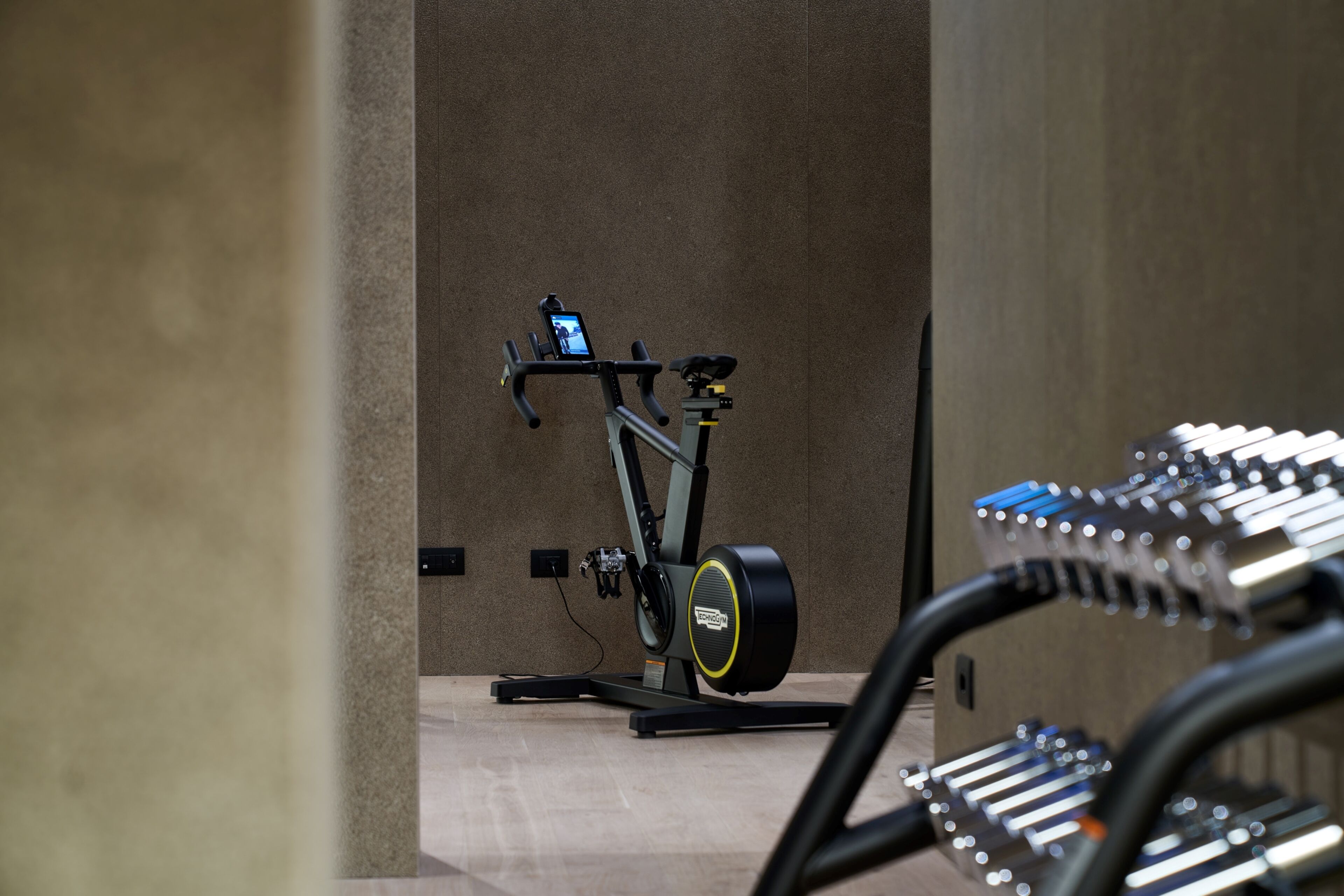 A stationary bike in a room with a concrete wall and a tiled floor.