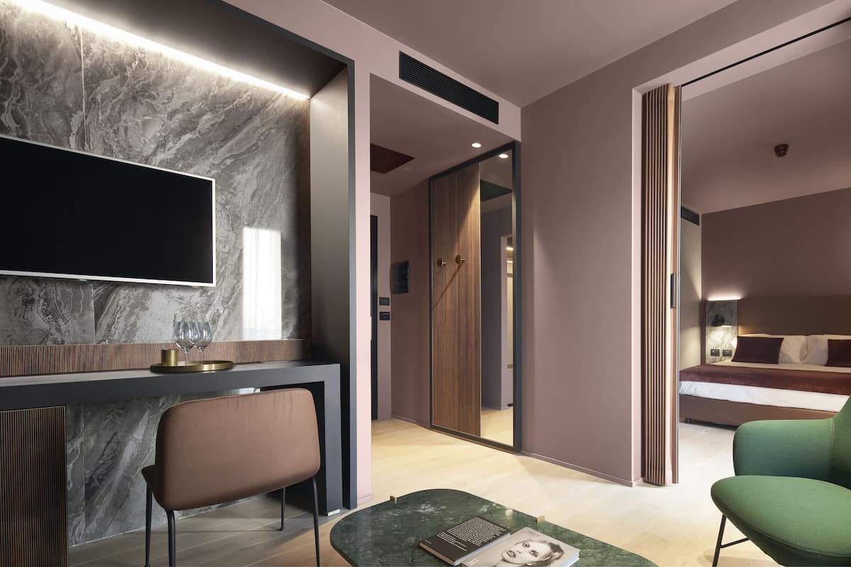A modern hotel room with a marble wall, a flat-screen TV, a wooden door, and a bed with pillows.