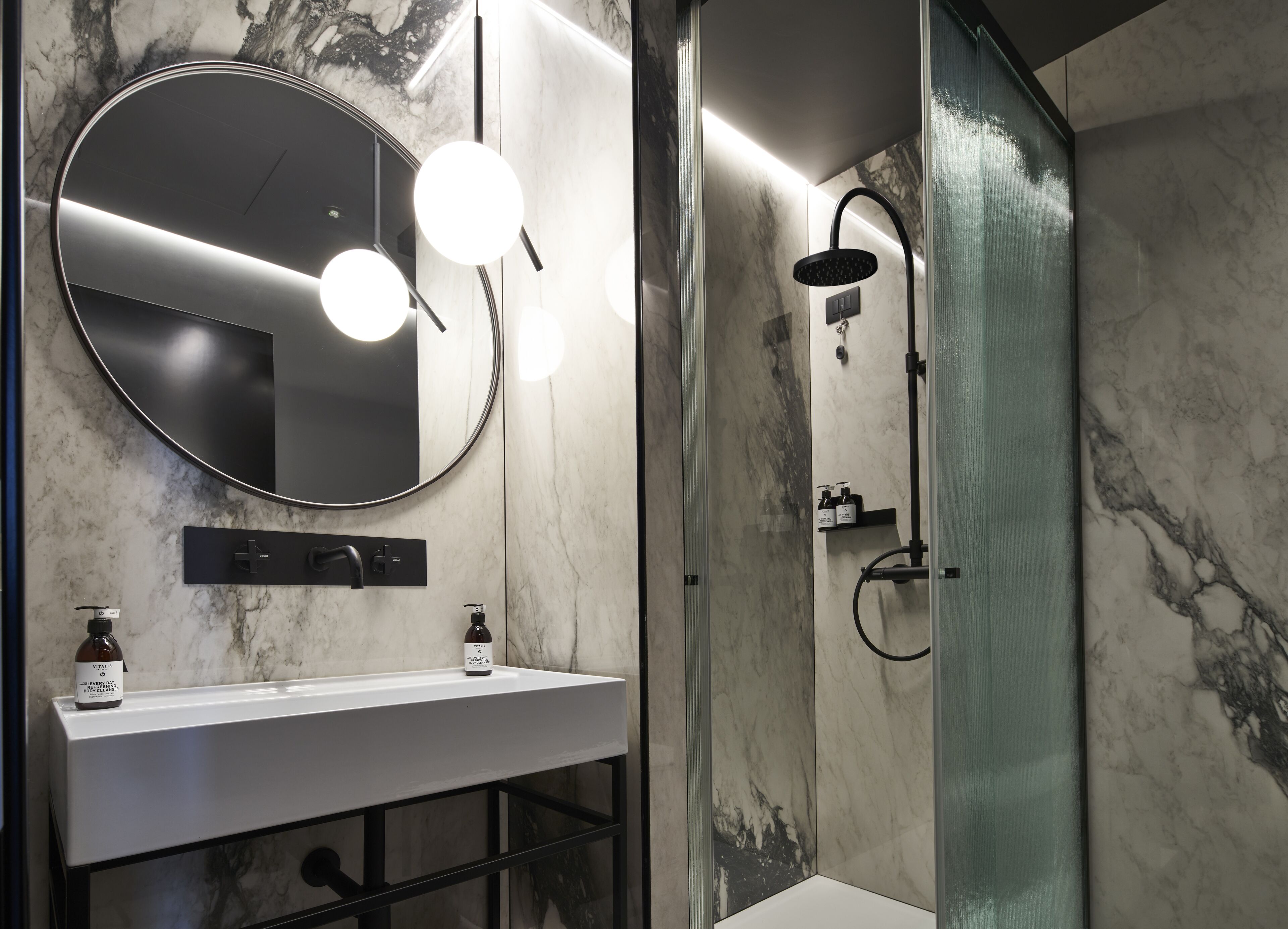 Un baño moderno con lavamanos de mármol, un espejo redondo y una zona de ducha con mampara de vidrio.