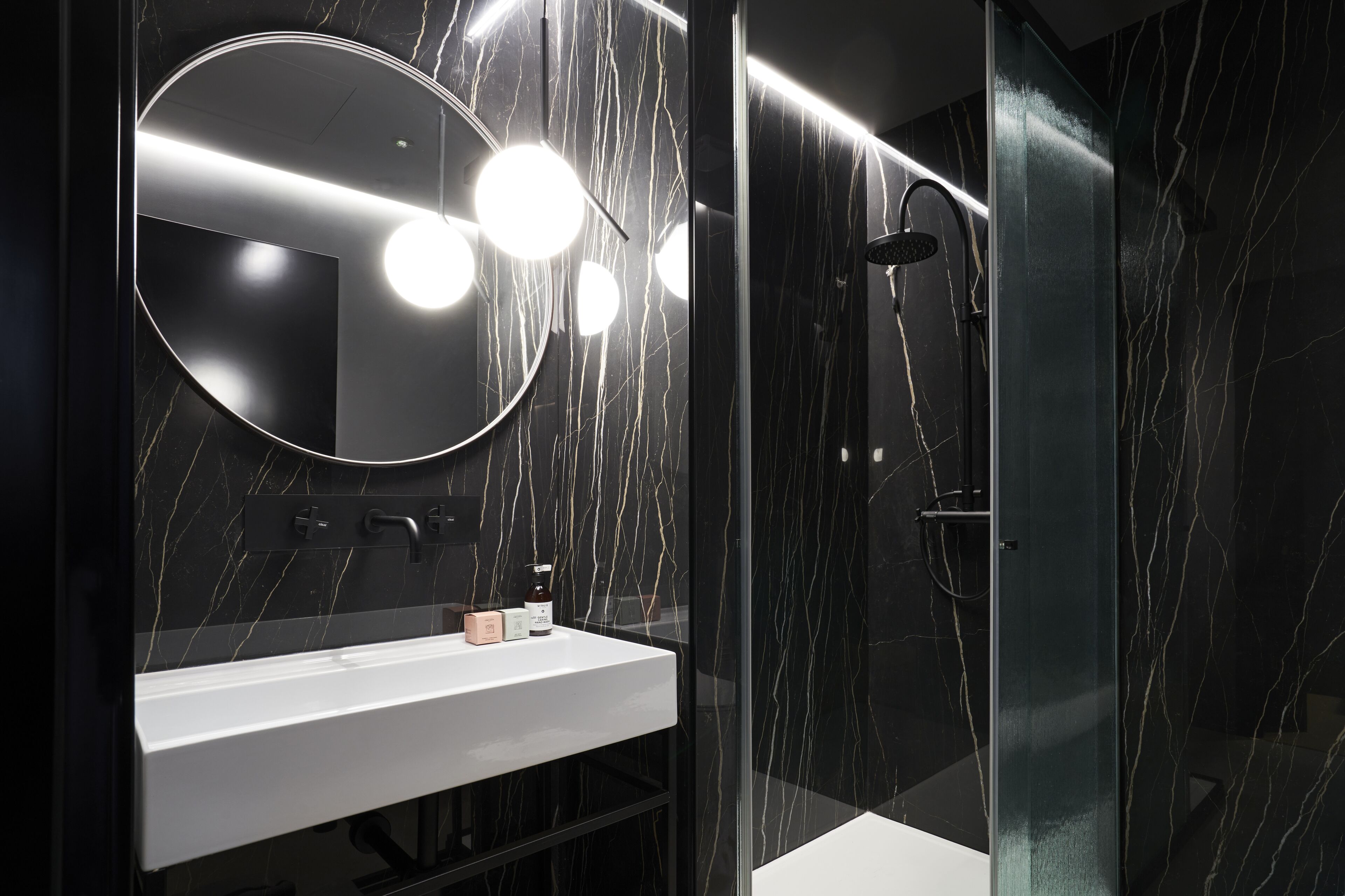 A modern bathroom with a white sink, a round mirror, and a glass-enclosed shower area.