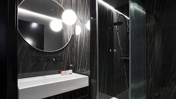 A modern bathroom with a white sink, a round mirror, and a glass-enclosed shower area.