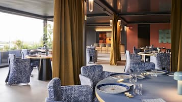 Un restaurante moderno con sillas de diseño azul estampada, mesas redondas y vistas a la ciudad.