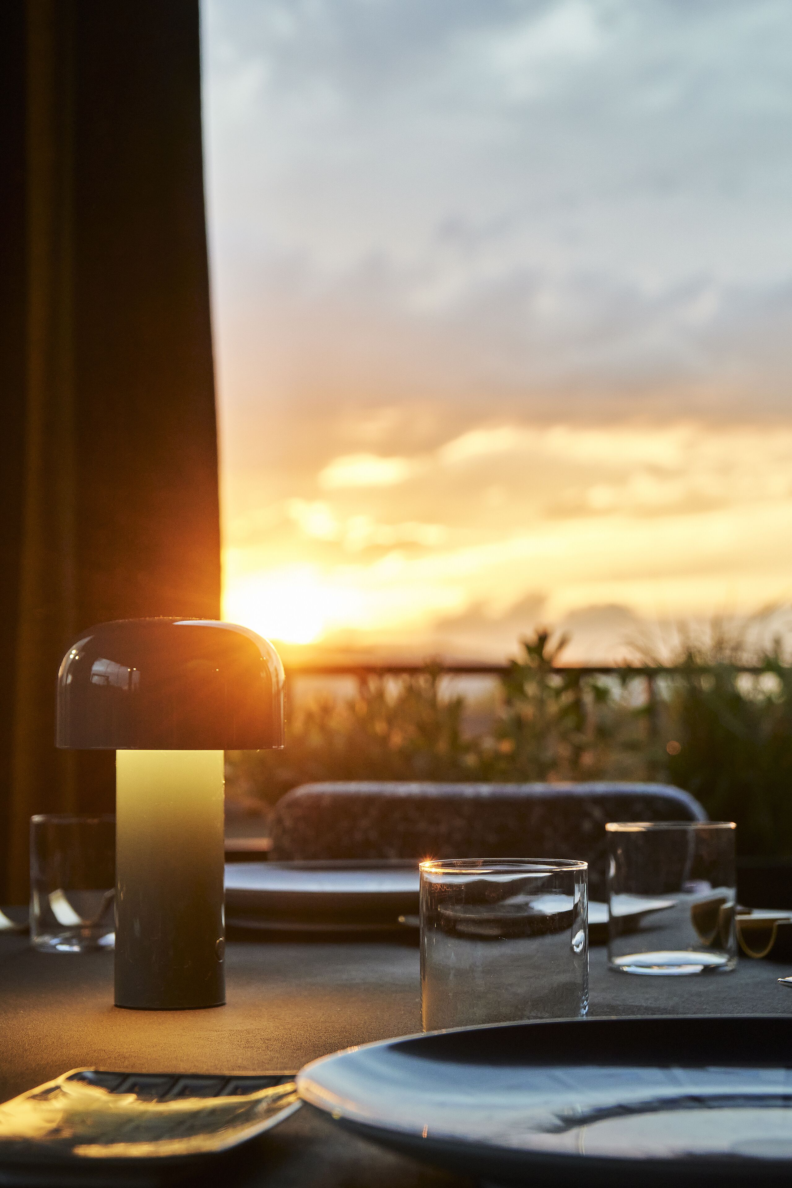 Une table dressée pour le dîner, avec une bougie, des verres et une vue sur un coucher de soleil.