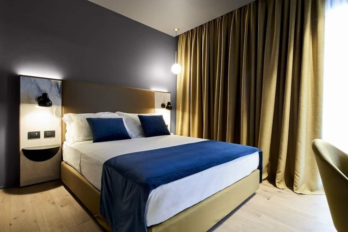 A modern hotel room with a large bed, bedside lamps, and a view of the outdoors through curtains.