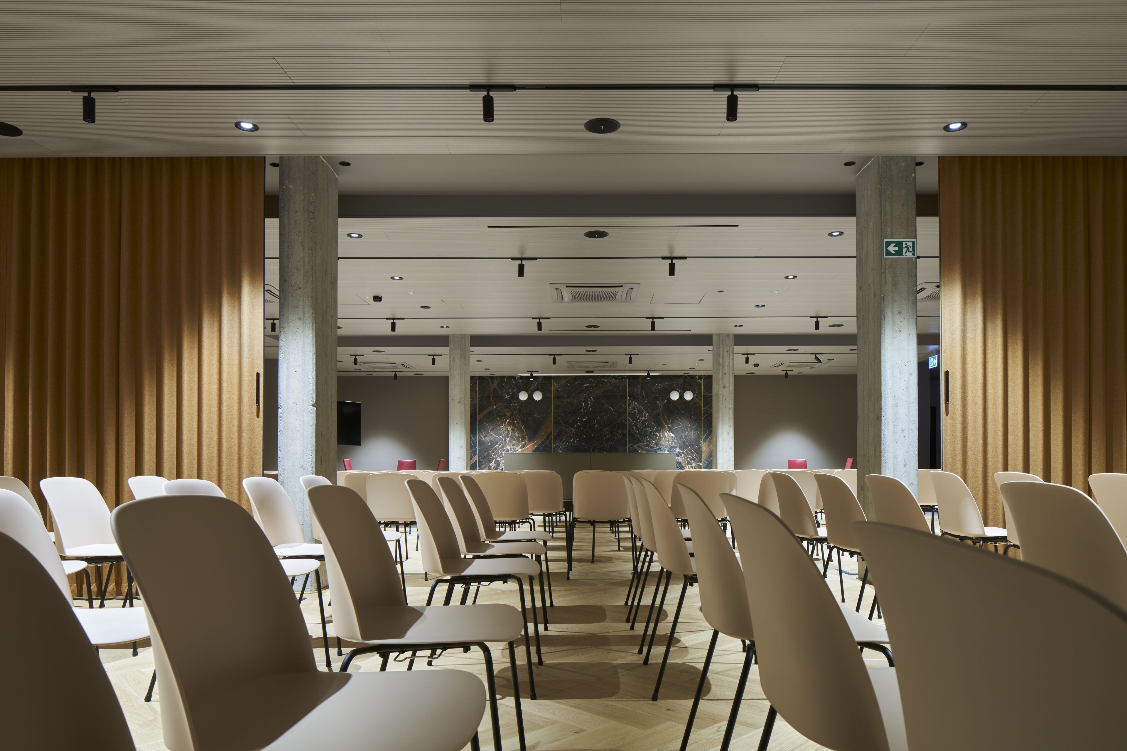 Ein Konferenzraum mit Reihen von Stühlen und Tischen, großen Fenstern und einer hohen Decke mit eingelassener Beleuchtung.