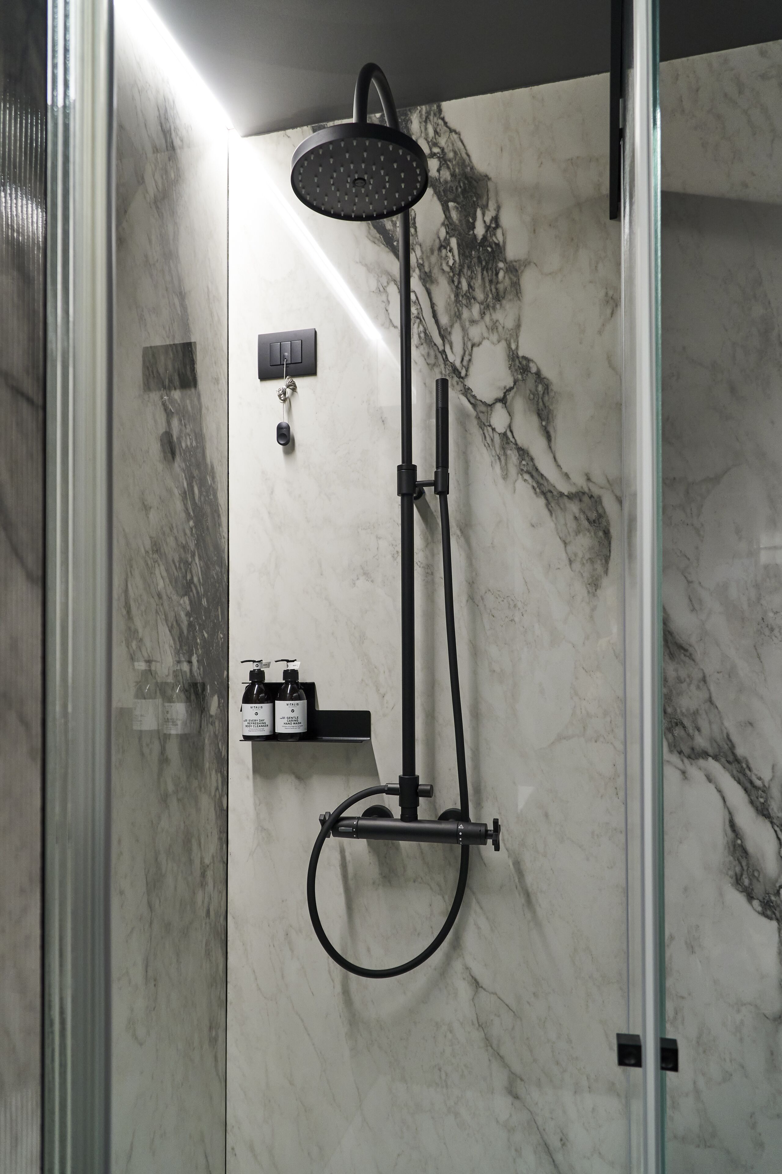 Une douche moderne dotée d’un pommeau de douche à main et d’un panneau de commande fixé au mur.