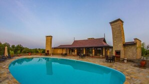A pool area with a stone patio, a building with a red roof, and outdoor seating. - Ol Pejeta Mansion (Nanyuki)