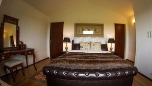 A bedroom with a large bed, a wooden desk, two chairs, a mirror, and a framed picture on the wall. - Ol Pejeta Mansion (Nanyuki)