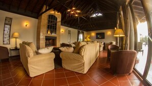 A spacious living area with a high ceiling, a fireplace, and large windows. - Ol Pejeta Mansion (Nanyuki)