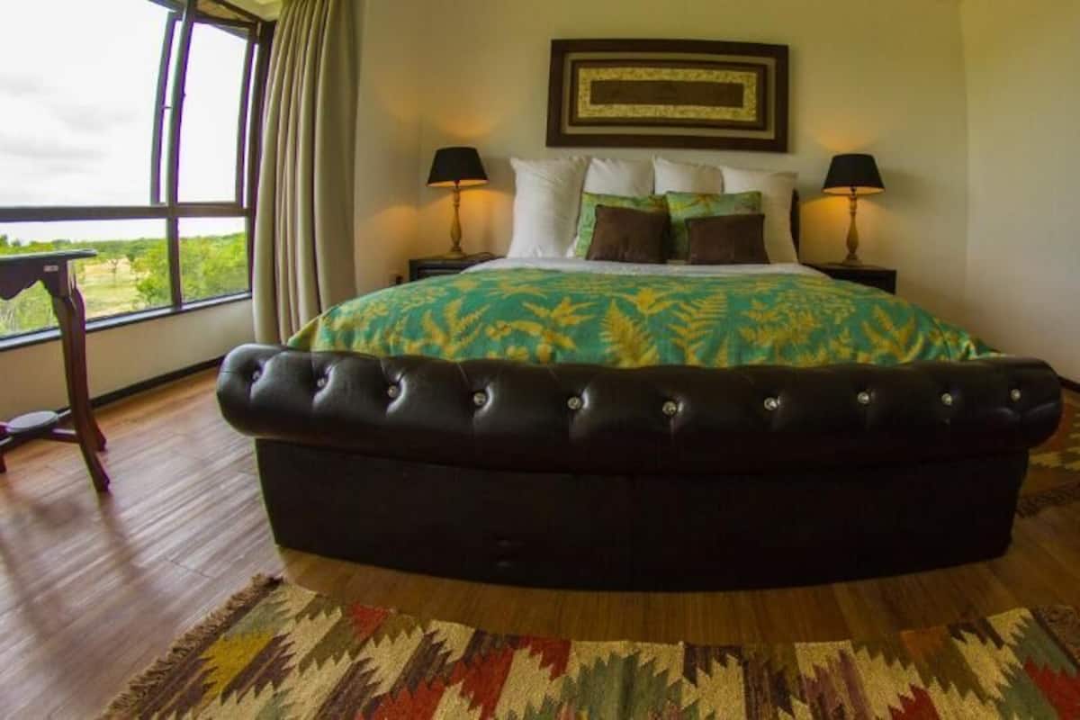Un dormitorio con una cama grande, dos lámparas de noche, una mesita de noche de madera, un aparador y vistas al exterior.