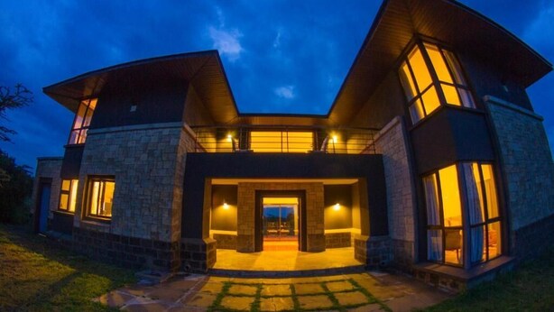A modern house with a stone facade, large windows, and a well-lit entrance. - Ol Pejeta Mansion (Nanyuki)