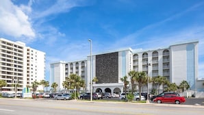 Un hôtel doté d’une façade moderne, de nombreux balcons et d’un parking où sont stationnées plusieurs voitures.
