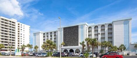 Un hotel con fachada moderna, varios balcones y un estacionamiento con varios automóviles.