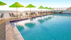 Une piscine avec des chaises longues et des parasols, une terrasse carrelée et une vue sur l’océan.