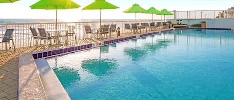Una piscina con sillas de descanso y sombrillas, un suelo de baldosas y vistas al océano.
