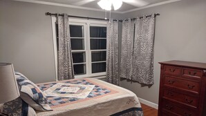 A bedroom with a bed, a dresser, a window with curtains, and a lamp. - Cozy lakeview home (Guntersville)