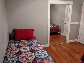 Ein Schlafzimmer mit einem Bett, einem roten Kissen und einer Steude. Eine Tür führt in einen anderen Raum.