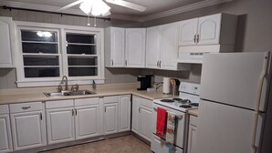 A kitchen with white cabinets, a stove, a refrigerator, a sink, and a window with blinds. - Cozy lakeview home (Guntersville)