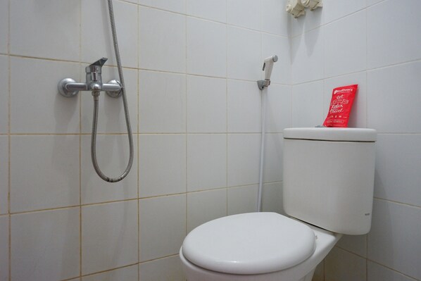 Um banheiro com vaso sanitário branco, chuveiro e uma embalagem vermelha sobre o reservatório.