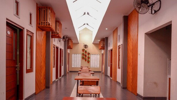 A corridor with wooden benches, a ceiling fan, and a wall-mounted fan. - Reddoorz Near Jogja Expo Center 2 (Banguntapan)