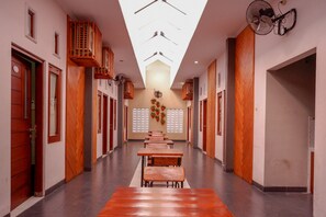 Um corredor com bancos de madeira, um ventilador de teto e um ventilador fixado na parede.
