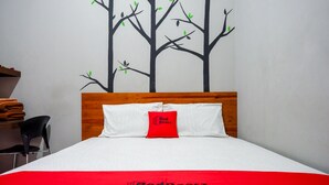 A neatly made bed with a red and white bedspread, a wooden headboard, and a wall mural of trees. - Reddoorz Near Jogja Expo Center 2 (Banguntapan)