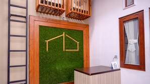 A room with a wooden desk, a green artificial grass wall, a wooden ladder, and a window with a curtain. - Reddoorz Near Jogja Expo Center 2 (Banguntapan)