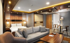 Una habitación de hotel moderna con cama, sofá y sillón, techo de madera y una pequeña mesa con un control remoto.