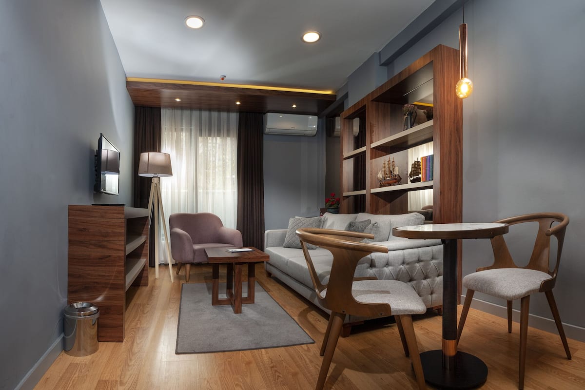 A modern living room with a grey sofa, wooden coffee table, and matching chairs. There is a bookshelf with decorative items and a TV mounted on the wall.
