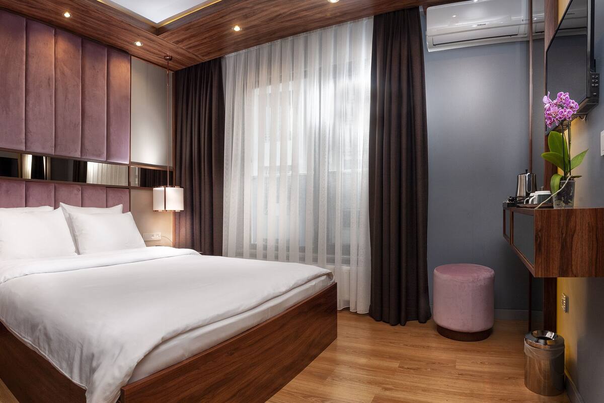 A modern hotel room with a large bed, wooden headboard, and a built-in wardrobe.