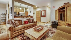 A living room with a brown leather sofa, a wooden coffee table, and a kitchen in the background.