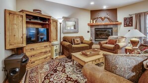 A cozy living room with a wooden entertainment unit, two sofas, a fireplace, and a patterned rug.