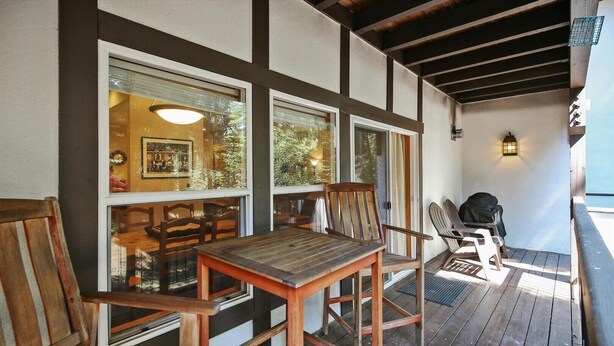 A wooden deck with a table and chairs, large windows, and a lantern.