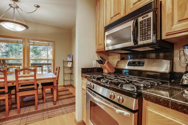 Una cocina con armarios de madera, una estufa a gas, un microondas y un comedor con mesa y sillas.