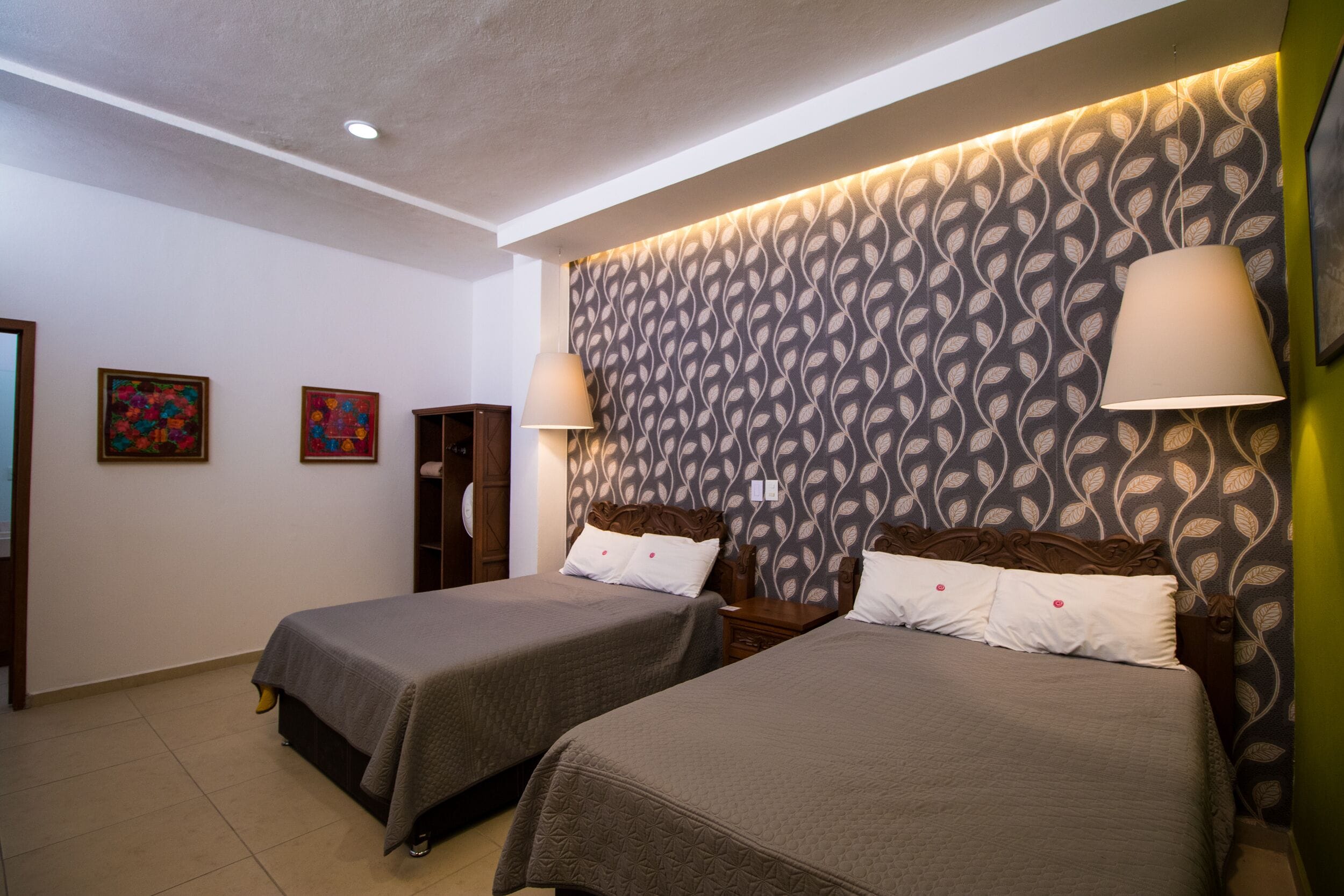 A hotel room with two beds, a patterned wallpaper, and a ceiling light.