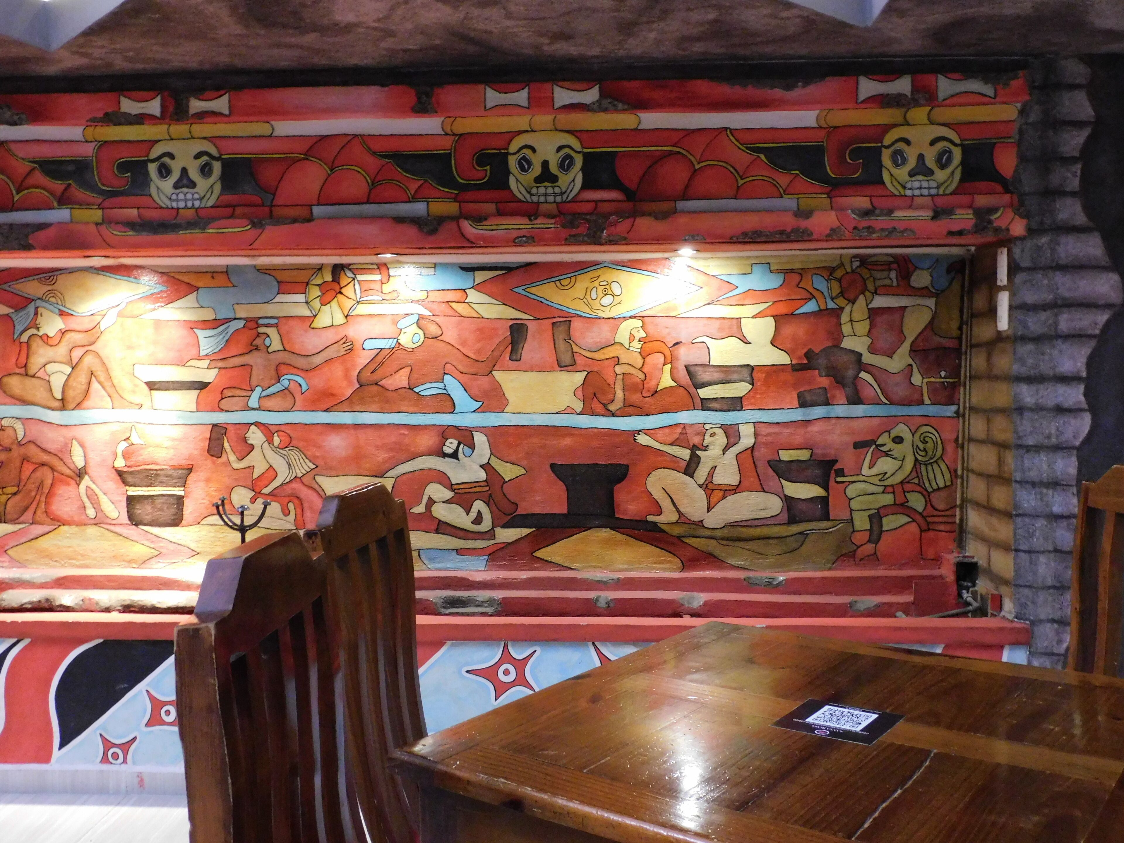 A restaurant interior with a mural on the wall, wooden chairs, and a table.