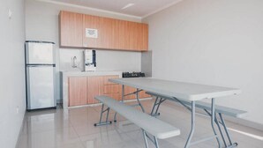 A compact kitchen with wooden cabinets, a white refrigerator, a sink, and a table with benches. - Reddoorz Plus Near Soekarno Hatta Airport Taman Mahkota (Tangerang)