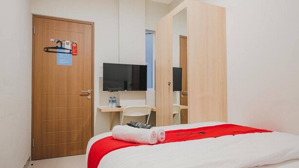 A hotel room with a bed, a desk, a chair, a TV, and a door with a safety sign. - Reddoorz Plus Near Soekarno Hatta Airport Taman Mahkota (Tangerang)