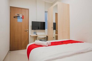 A hotel room with a bed, a desk, a chair, a TV, and a door with a safety sign.