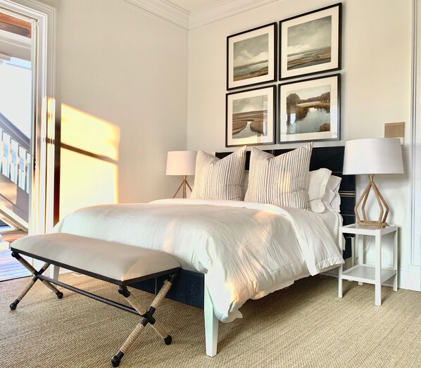 A bedroom with a large bed, bedside tables with lamps, and a bench. There are framed pictures on the wall.