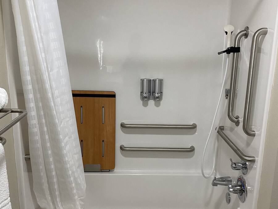 A modern bathroom with a bathtub, shower, grab bars, and a towel rack.