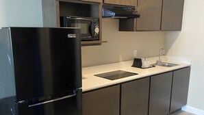 A modern kitchen with dark wooden cabinets, a black refrigerator, a microwave, and a sink. - Hotel DeSoto (Olive Branch)