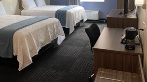 A hotel room with two beds, a desk, a chair, a coffee maker, and a window with curtains. - Hotel DeSoto (Olive Branch)