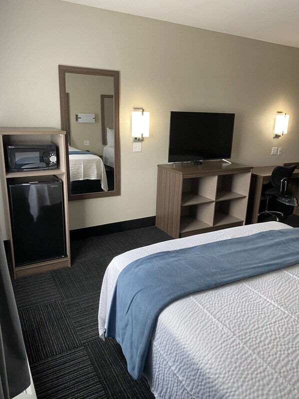 A hotel room with a bed, a desk with a flat-screen TV, a microwave, and a refrigerator. - Hotel DeSoto (Olive Branch)