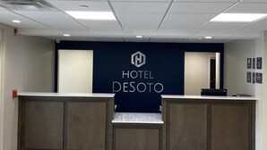 A hotel reception area with a modern design, featuring a reception desk, a digital screen, and a sign that reads "HOTEL DESOTO". - Hotel DeSoto (Olive Branch)