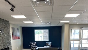 A spacious lobby with a dark blue wall, a stone fireplace, two patterned chairs, a black sofa, and a wooden floor. - Hotel DeSoto (Olive Branch)