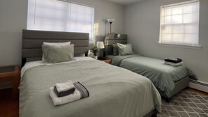 Un dormitorio moderno con dos camas, una mesita de noche, una lámpara y una ventana.