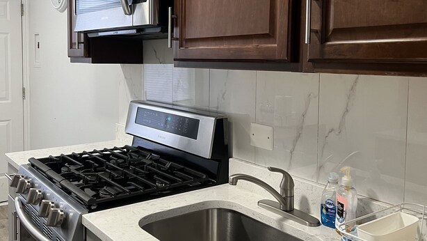 Una cocina con armarios de madera oscura, electrodomésticos de acero inoxidable, un microondas, una estufa y un fregadero.