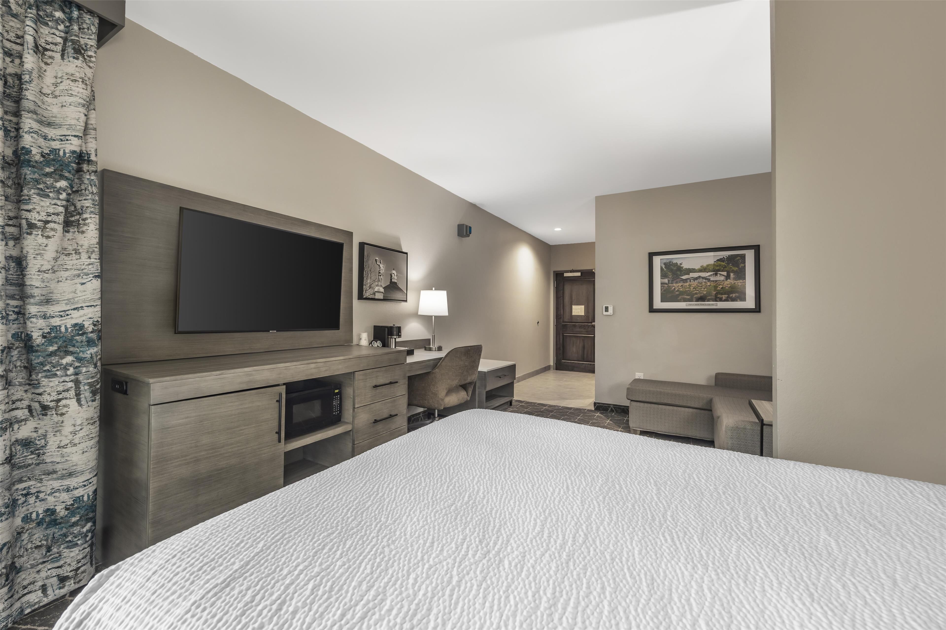 Habitación de hotel con una cama grande, un televisor de pantalla plana montado en la pared, un escritorio con una silla y un armario pequeño.