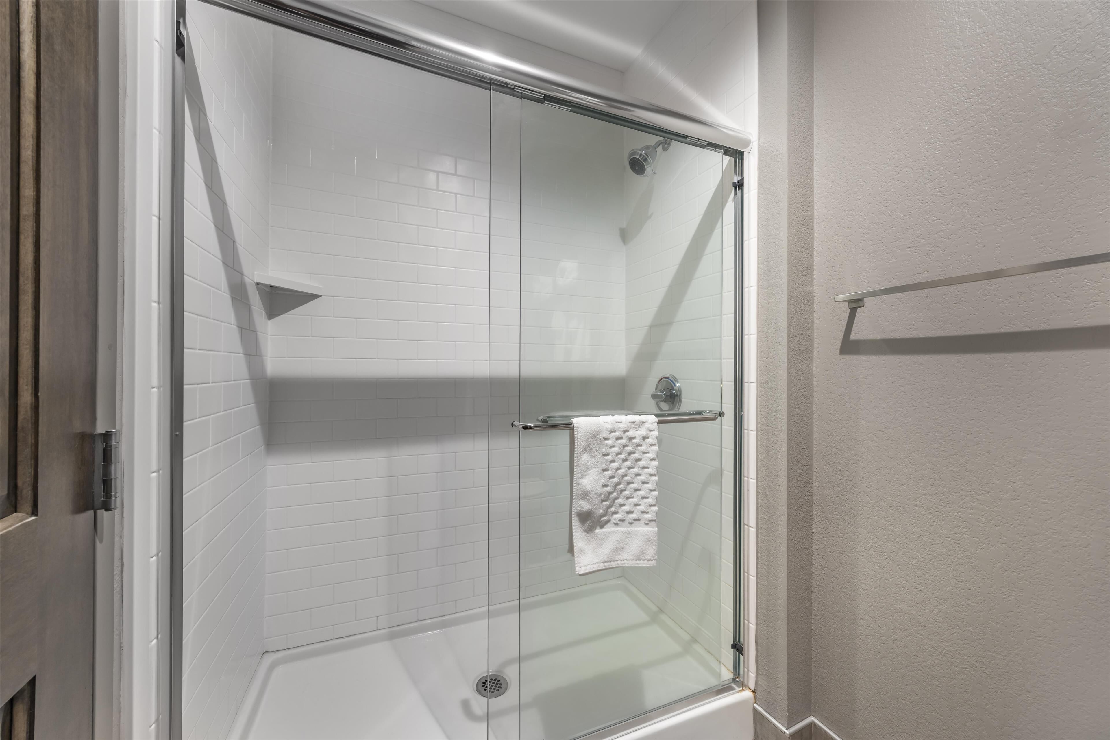 Une douche fermée par des parois de verre, avec des murs recouverts de carreaux blancs et une serviette blanche suspendue à un porte-serviettes en métal.